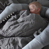 A sleeping child nestled in soft gray cartoon baby bedding, featuring a pillow that wraps around them, designed by Baby Bliss Haven for both fun and safety.